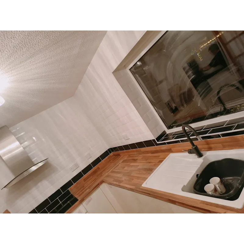 L-shaped kitchen with white and black accent tiles and wooden worktop