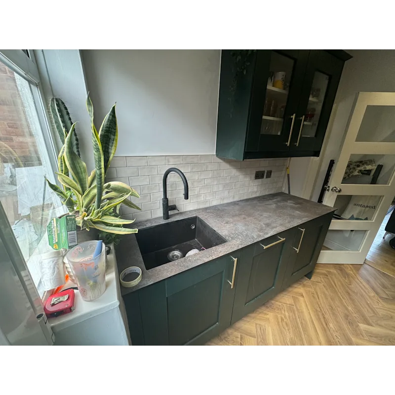 Kitchen with dark green cabinets, cream subway tile, and plants